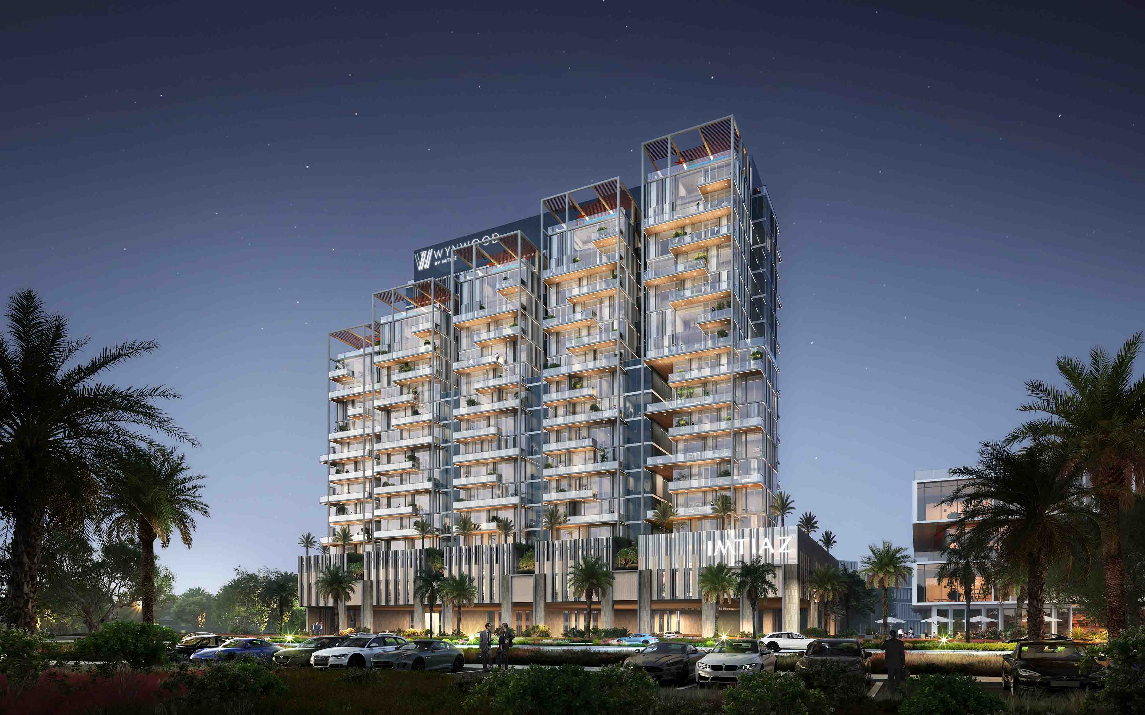 Wynwood By Imtiaz A modern multi-story building with glass balconies, surrounded by palm trees and illuminated at night.